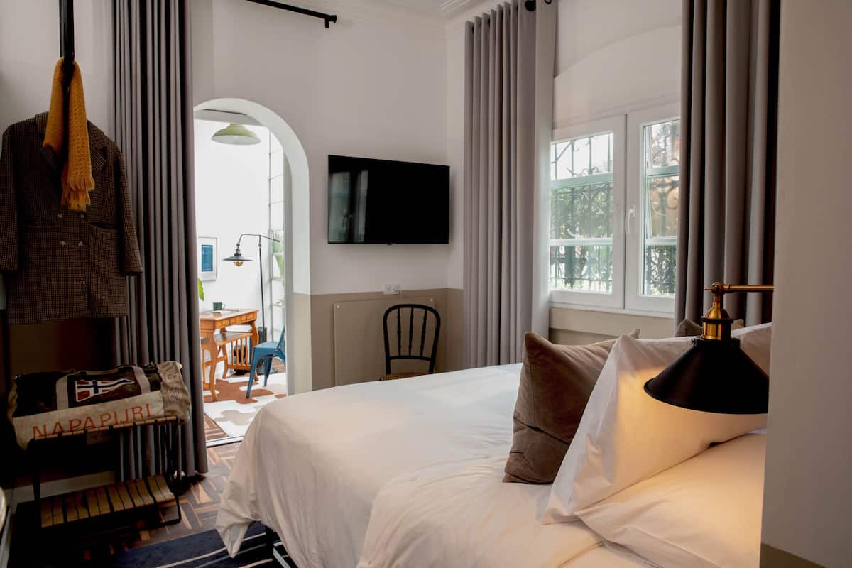 A hotel room with a bed, a television mounted on the wall, a chair, and a window with curtains.