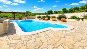 Ein Pool mit einer Steindekke, umgeben von Liegestühlen und einer Pergola.
