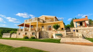 Ein zweistöckiges Steinhaus mit Balkon, einem kleinen Anbau und einem gepflasterten Auffahrt.