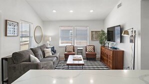 Un salon avec un canapé gris, une table basse, un meuble en bois et un téléviseur fixé au mur.
