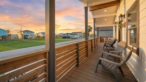 Un espace extérieur abrité, doté d’un plancher en bois et de fauteuils Adirondack, qui offre une vue sur une pelouse et des maisons.
