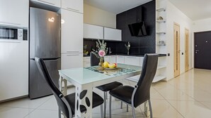 A modern kitchen with a stainless steel refrigerator, white cabinets, a glass dining table, and black chairs. - Comfortable apartments  (Minsk)
