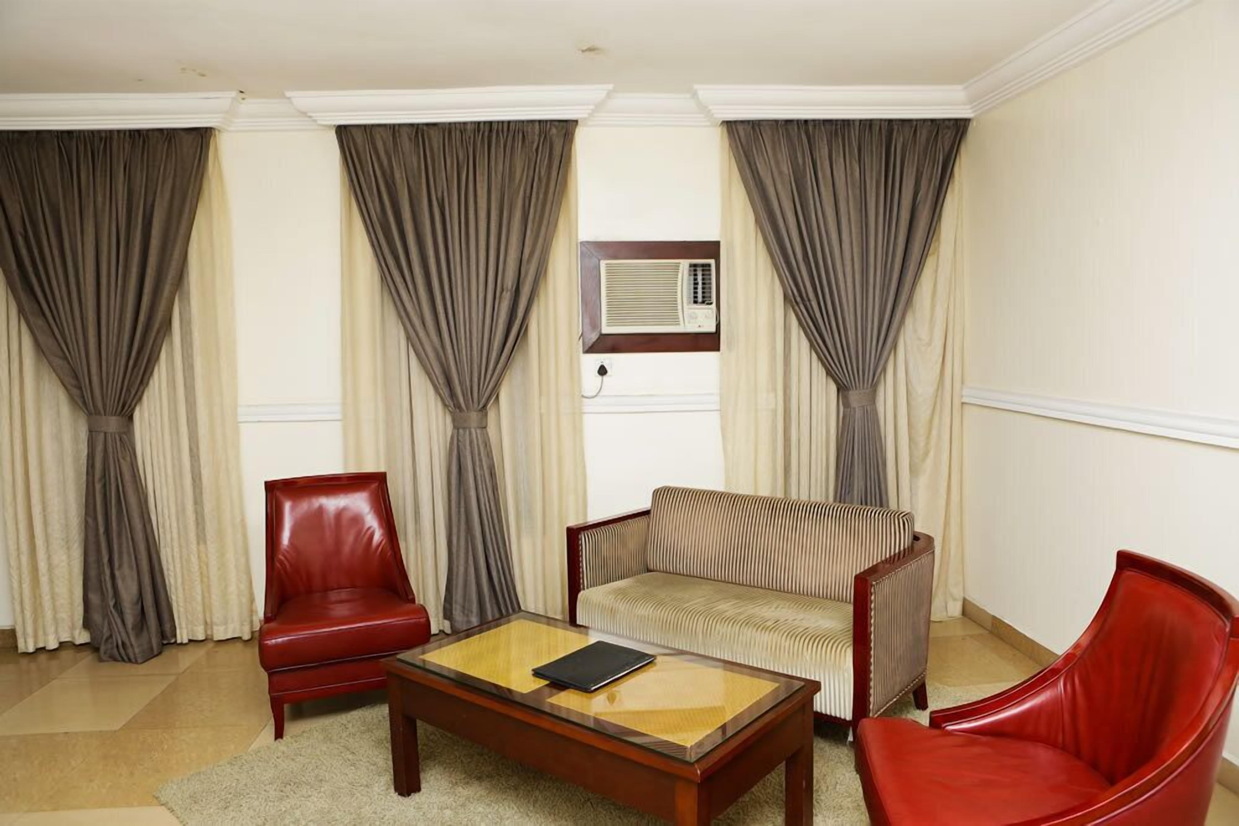 Una habitación con un sillón de cuero rojo, un sofá a rayas y una mesa de centro de madera.