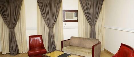 Una habitación con un sillón de cuero rojo, un sofá a rayas y una mesa de centro de madera.