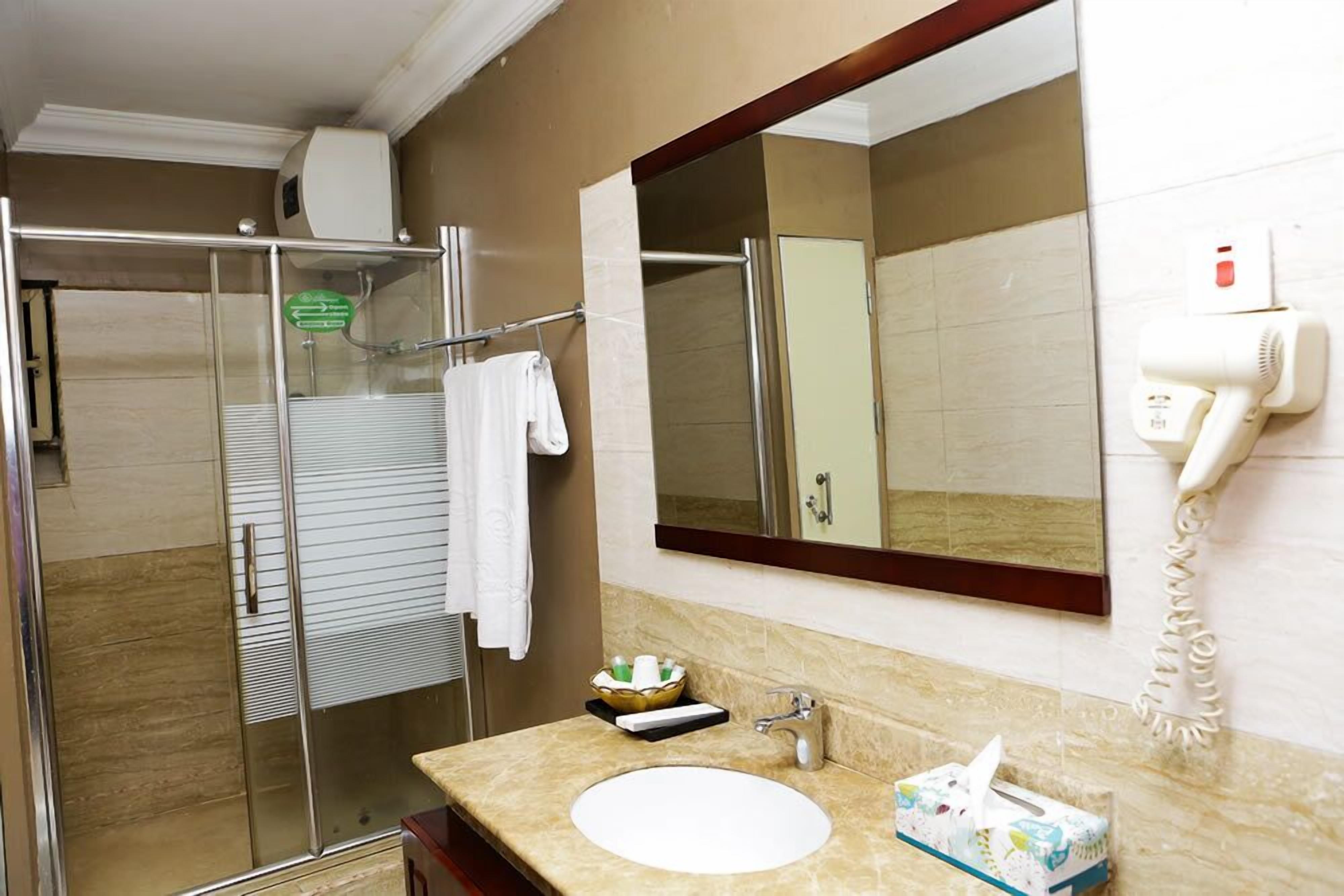 Un baño con cabina de ducha de vidrio, un lavamanos con espejo y un secador de pelo montado en la pared.