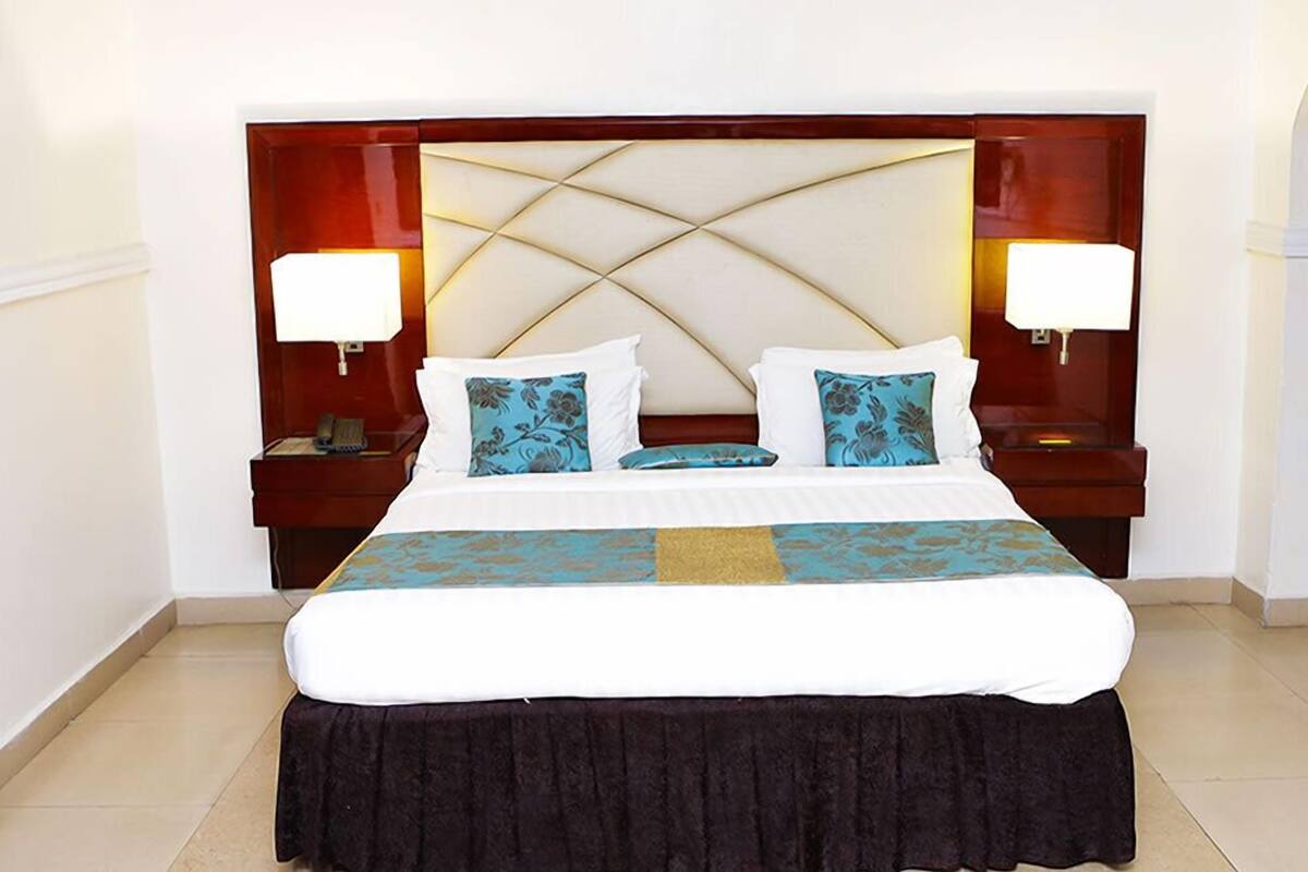 Een hotelkamer met een groot bed, twee nachtkastjes en een hoofdeinde met een geometrisch patroon.