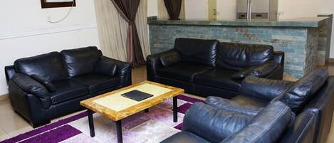 A living room with two black leather sofas, a wooden coffee table, and a purple rug.