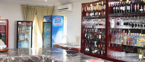 Una zona de bar con encimera de mármol, un refrigerador y estantes llenos de botellas y vasos.
