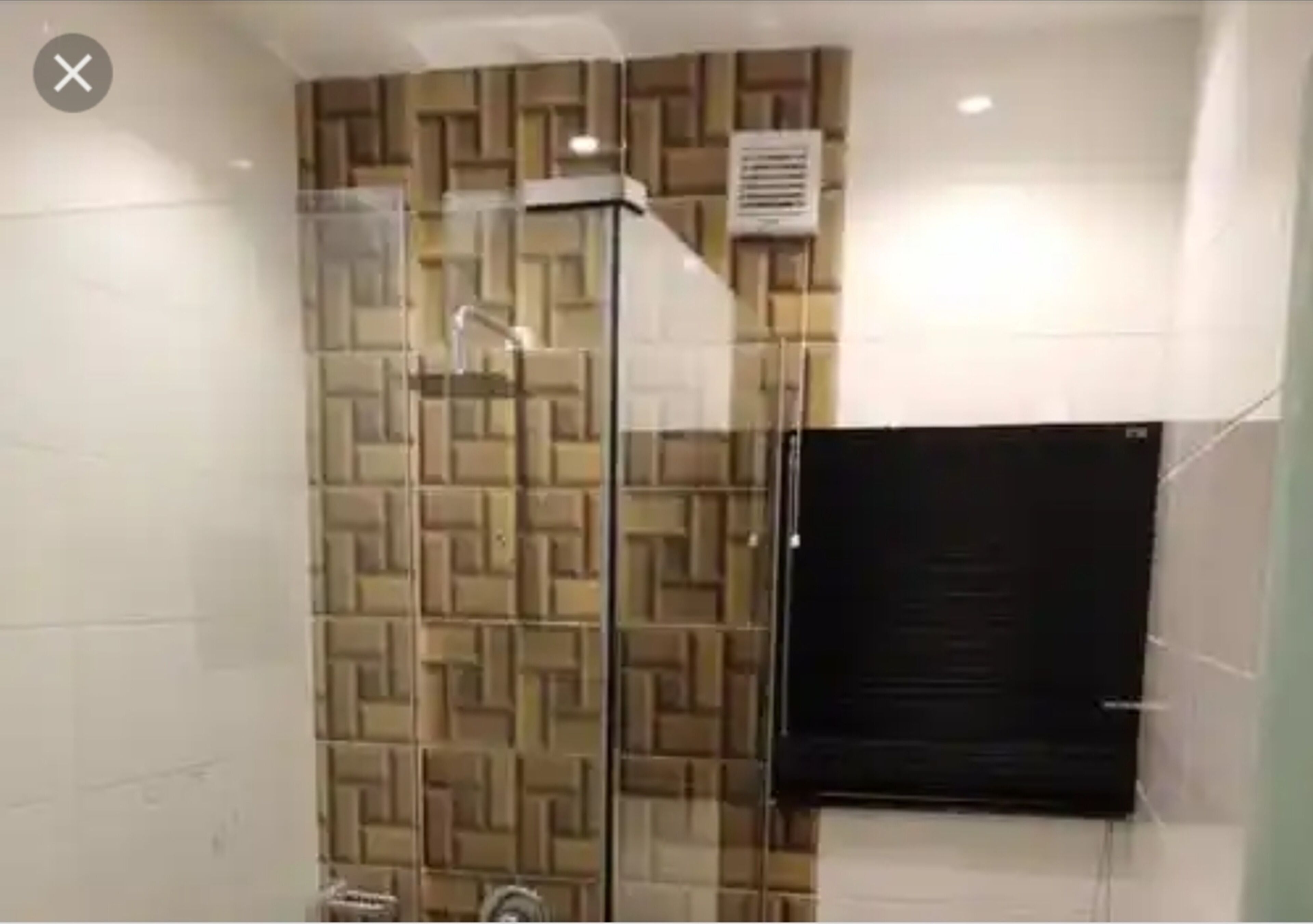A bathroom with a glass shower enclosure, a patterned wall, and a black towel rack.