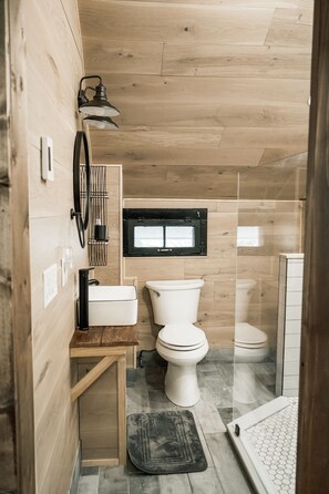 Ein kleines, hölzernes Badezimmer mit Toilette, Waschbecken und Duschbereich.