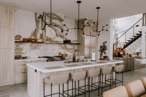 A modern kitchen with marble backsplash, pendant lighting, and a central island with bar stools.