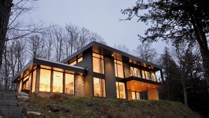 A modern two-story house with large windows and a stone exterior, surrounded by trees and a stone staircase.