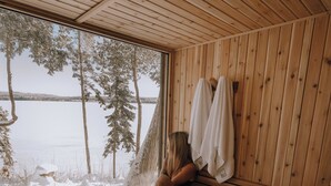 A wooden sauna with a bench and a bench seat, a towel rack, and a large window overlooking a snowy landscape.