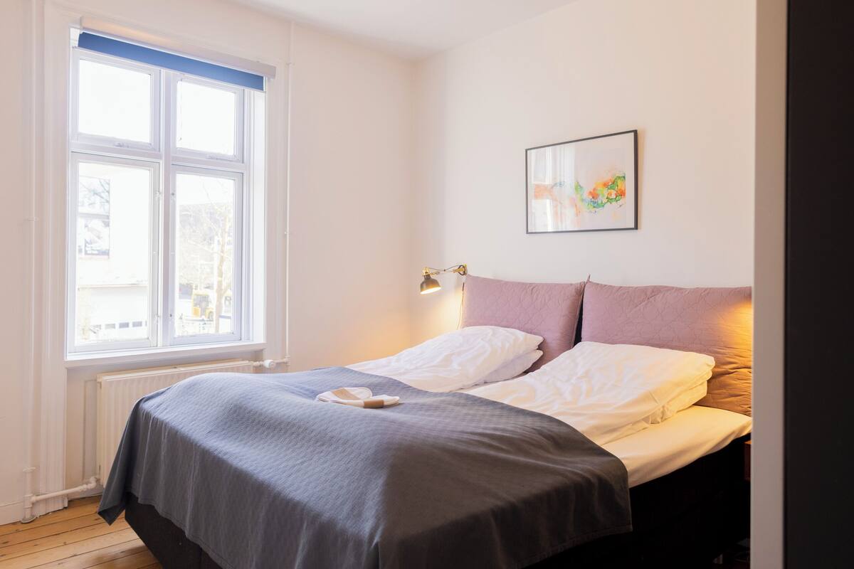 A bedroom with a bed, a window, and a wall-mounted light fixture.