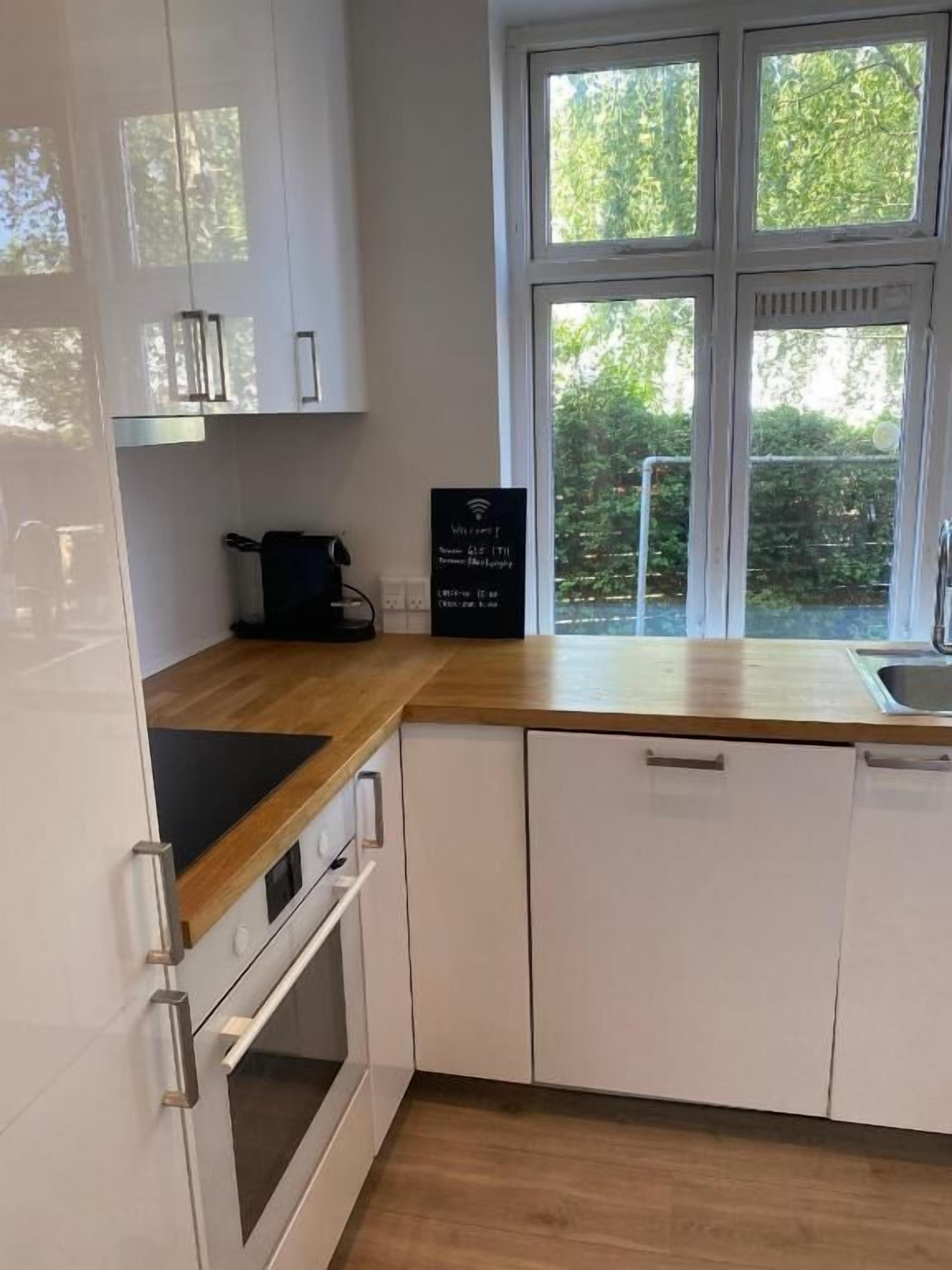 Ett modernt kök med vita skåp, en träbänkskiva och ett fönster med utsikt över grönområden.