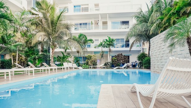 A pool area with lounge chairs, palm trees, and a multi-story building in the background.