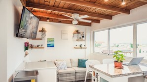 A modern kitchen with a wooden ceiling, a built-in fridge, a dining area with a laptop, and a large window offering a view of the city.