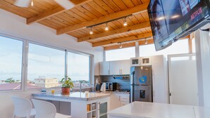 A modern kitchen with white cabinetry, a stainless steel refrigerator, a microwave, and a large window offering a view of the city.