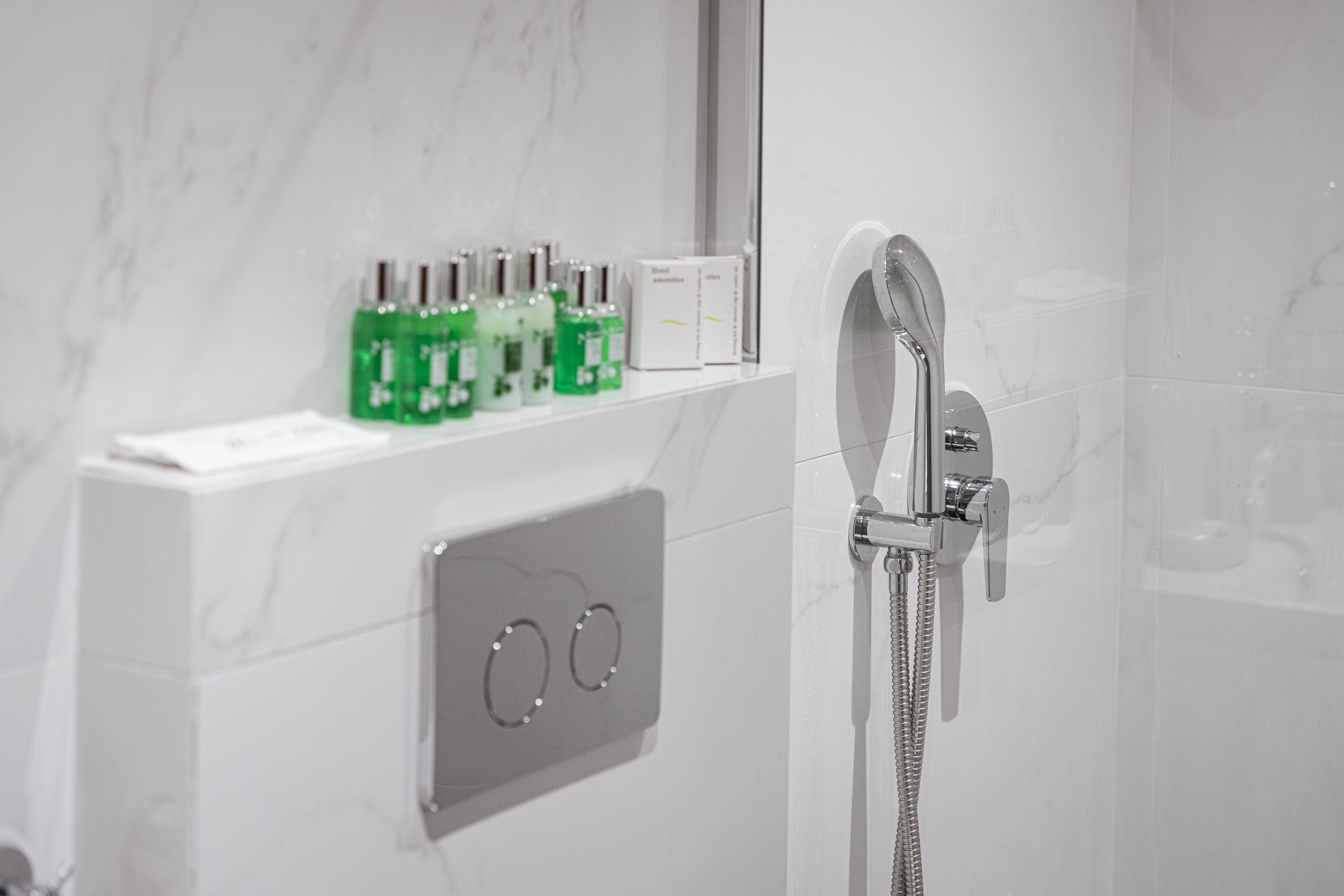 Une salle de bain moderne avec une douche, un panneau de commande et une étagère sur laquelle sont posées des bouteilles vertes.