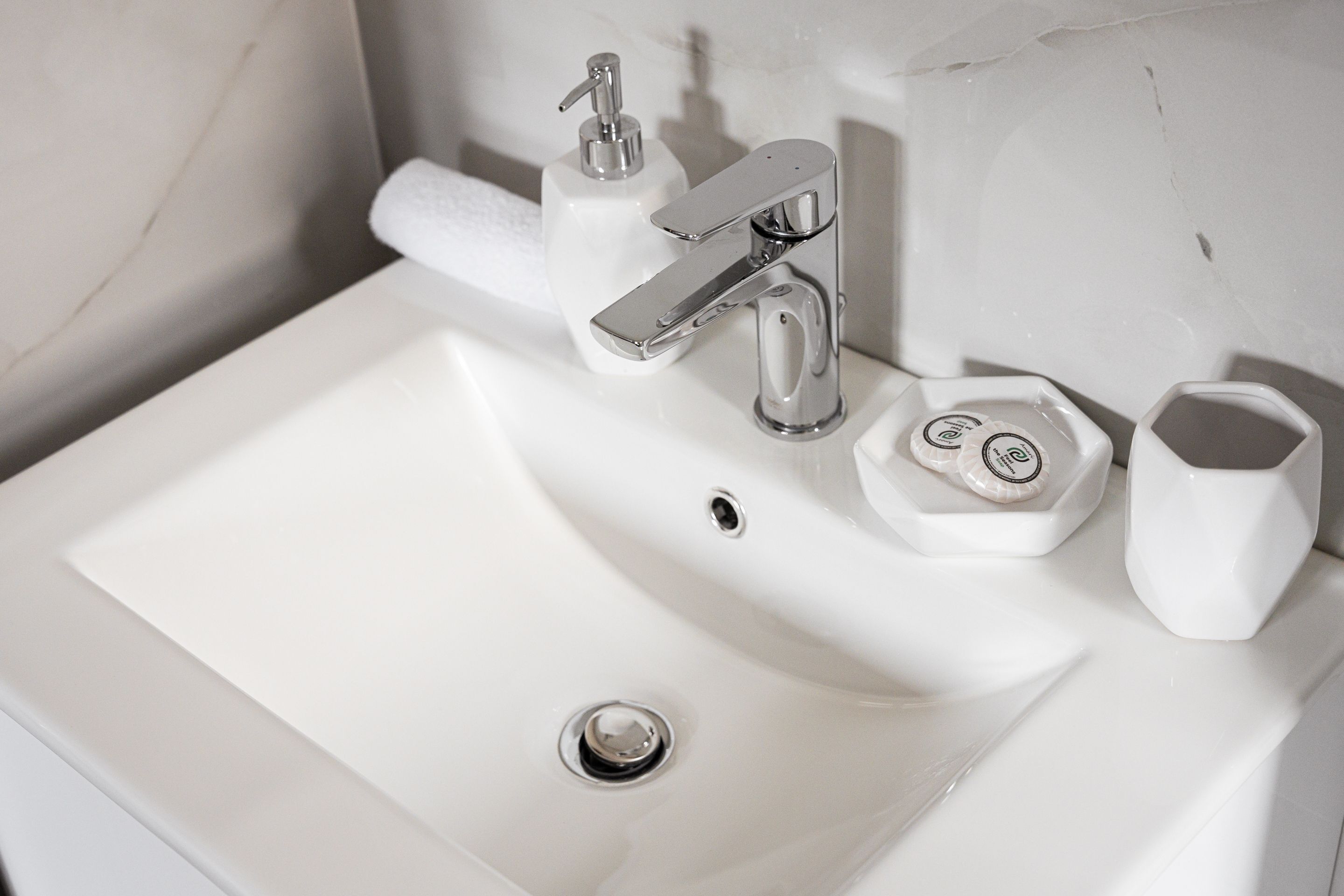 A white bathroom sink with a chrome faucet, a soap dispenser, and a toilet paper holder.
