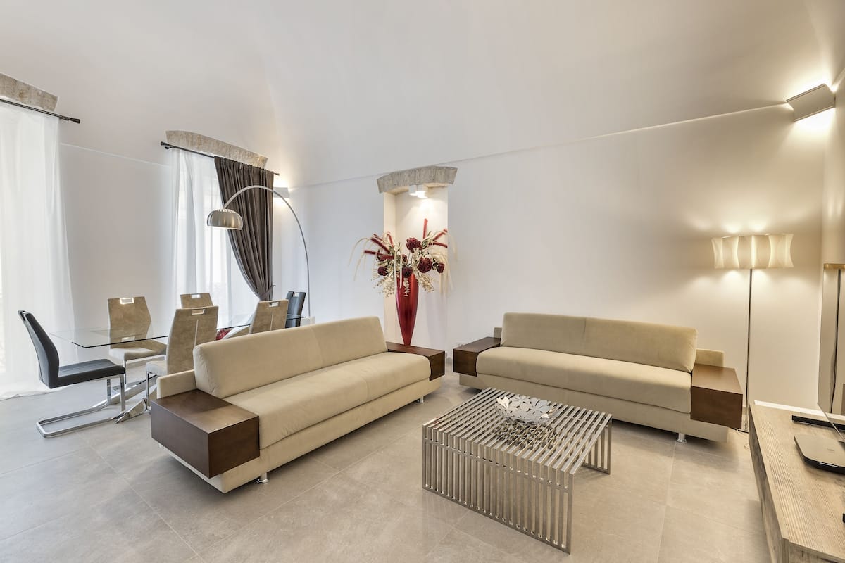 A modern living room with a sofa, coffee table, and a dining area with chairs and a glass table.