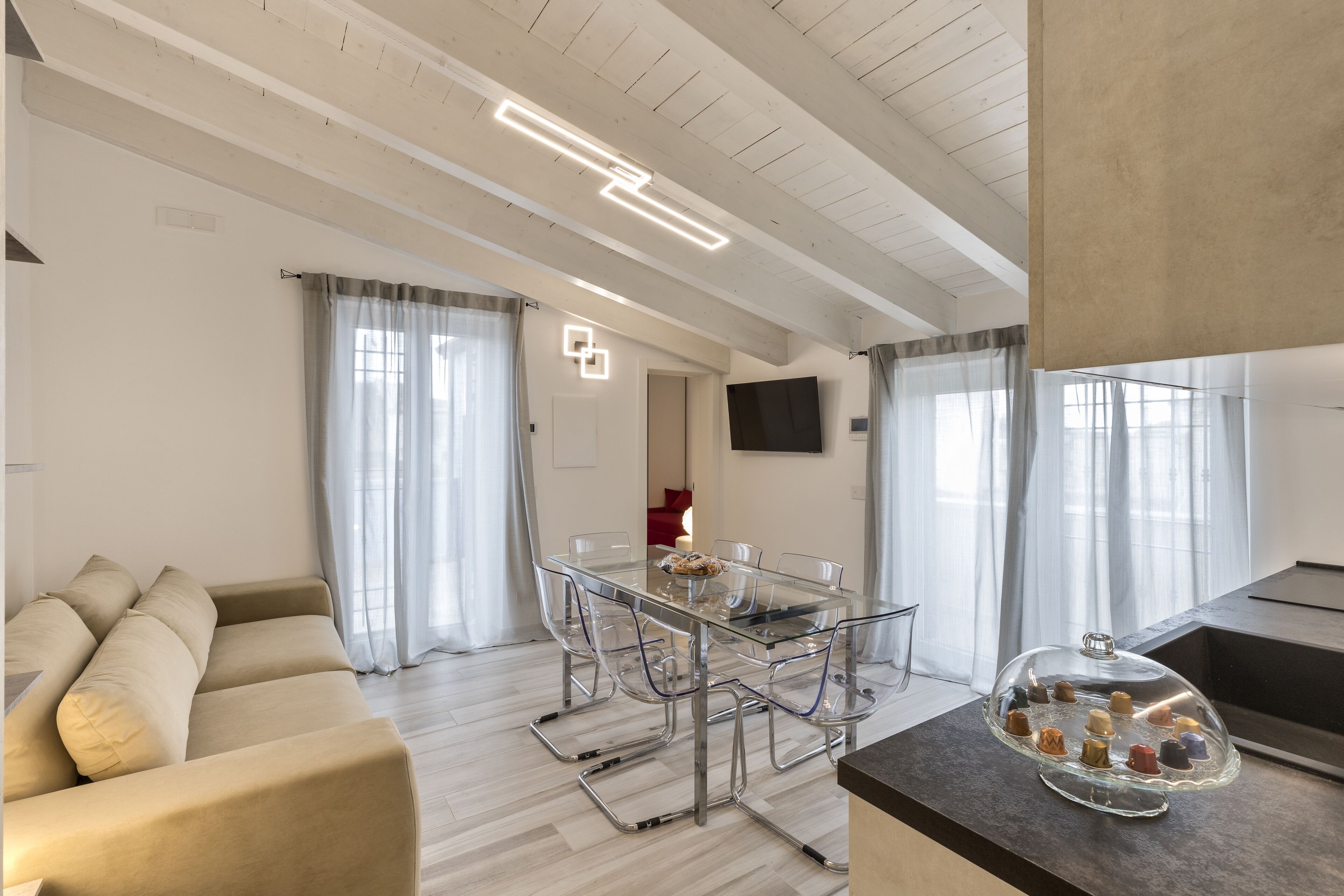 Una sala moderna con una mesa de comedor de vidrio, un sofá beige y una zona de cocina con encimera y vitrina de vidrio.