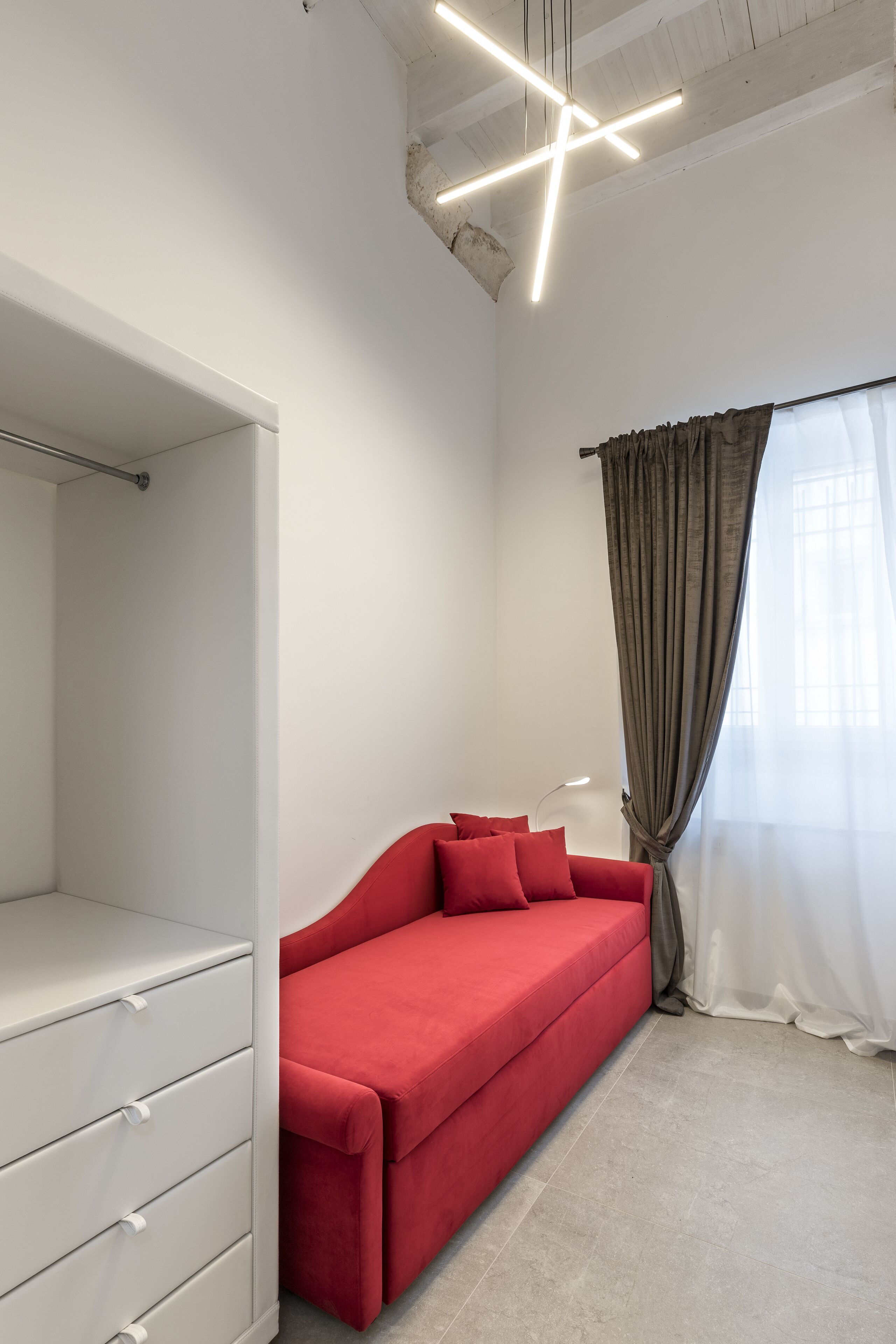 A modern room with a red sofa, a white wardrobe, and a large window with curtains.