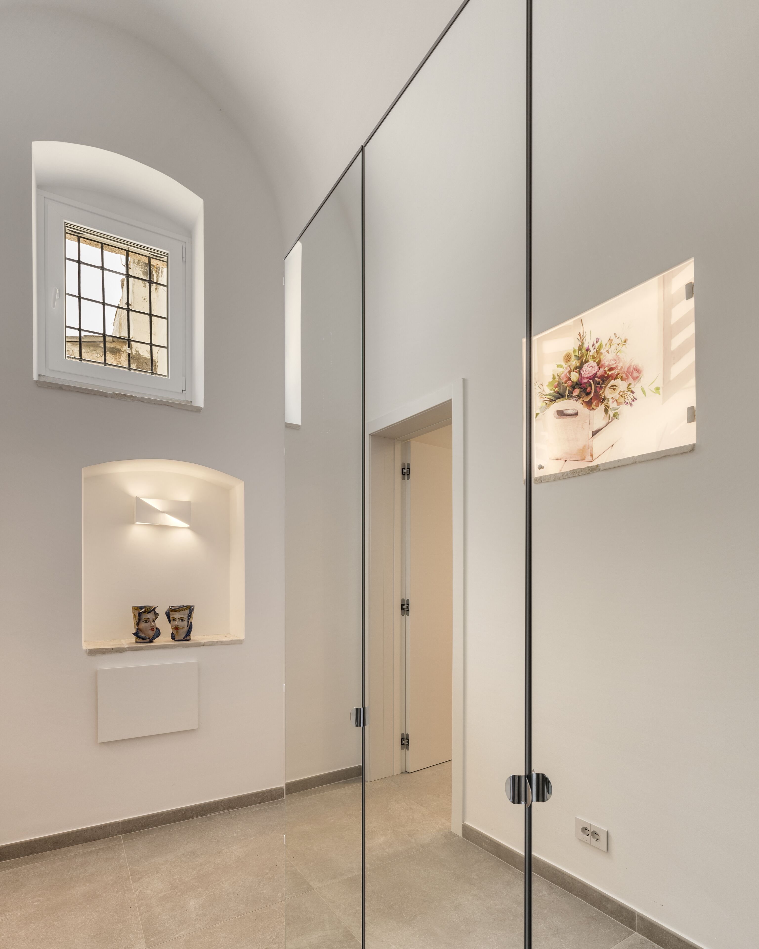 A modern hallway with a glass door, a small window with a grid pattern, and a wall-mounted artwork.