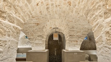 Explore a unique underground space with a vaulted ceiling and smooth stone walls, featuring a central passageway and a cozy alcove with a bench.