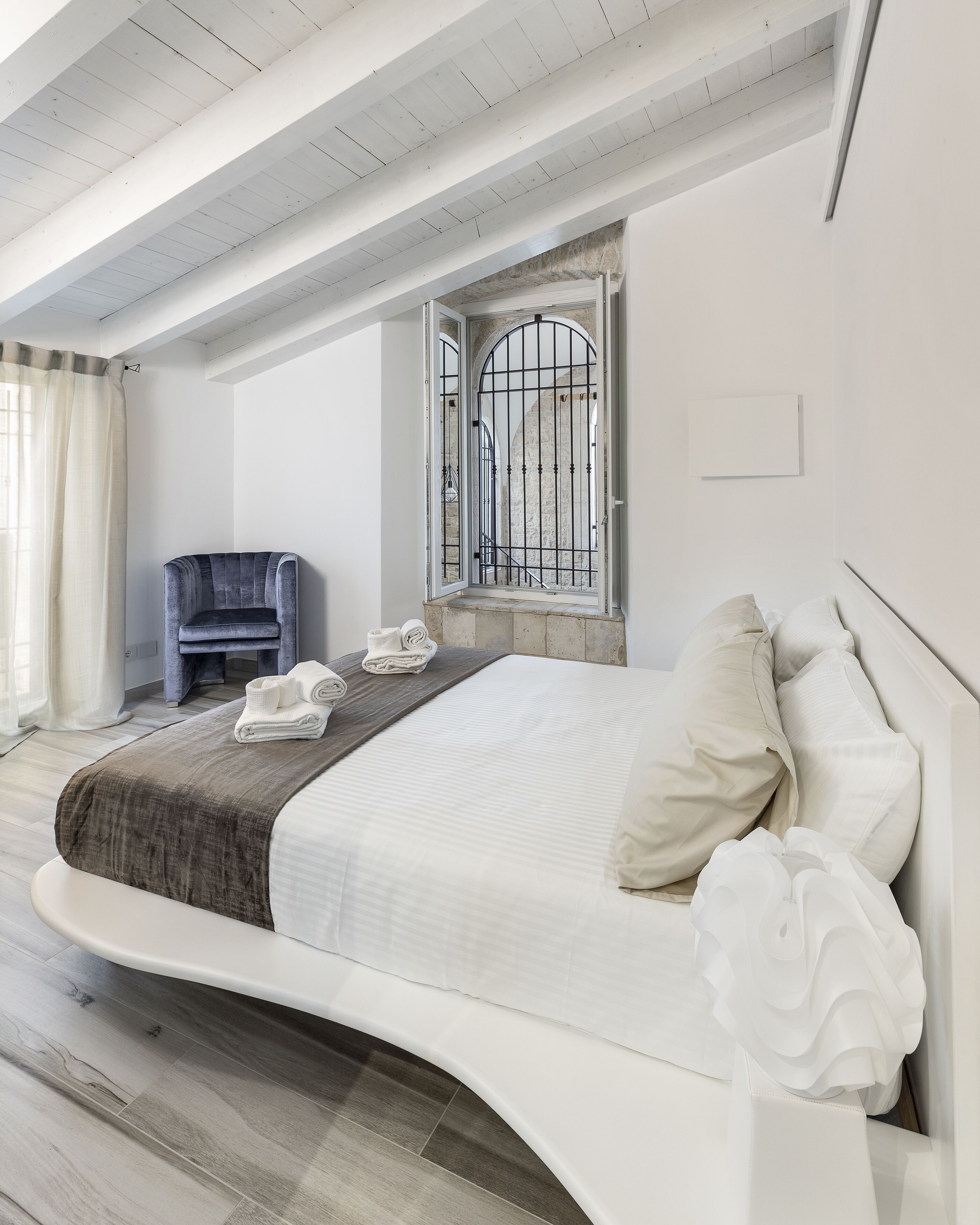 Een moderne slaapkamer met een gebogen bed, een stoel en een raam met metalen tralies.