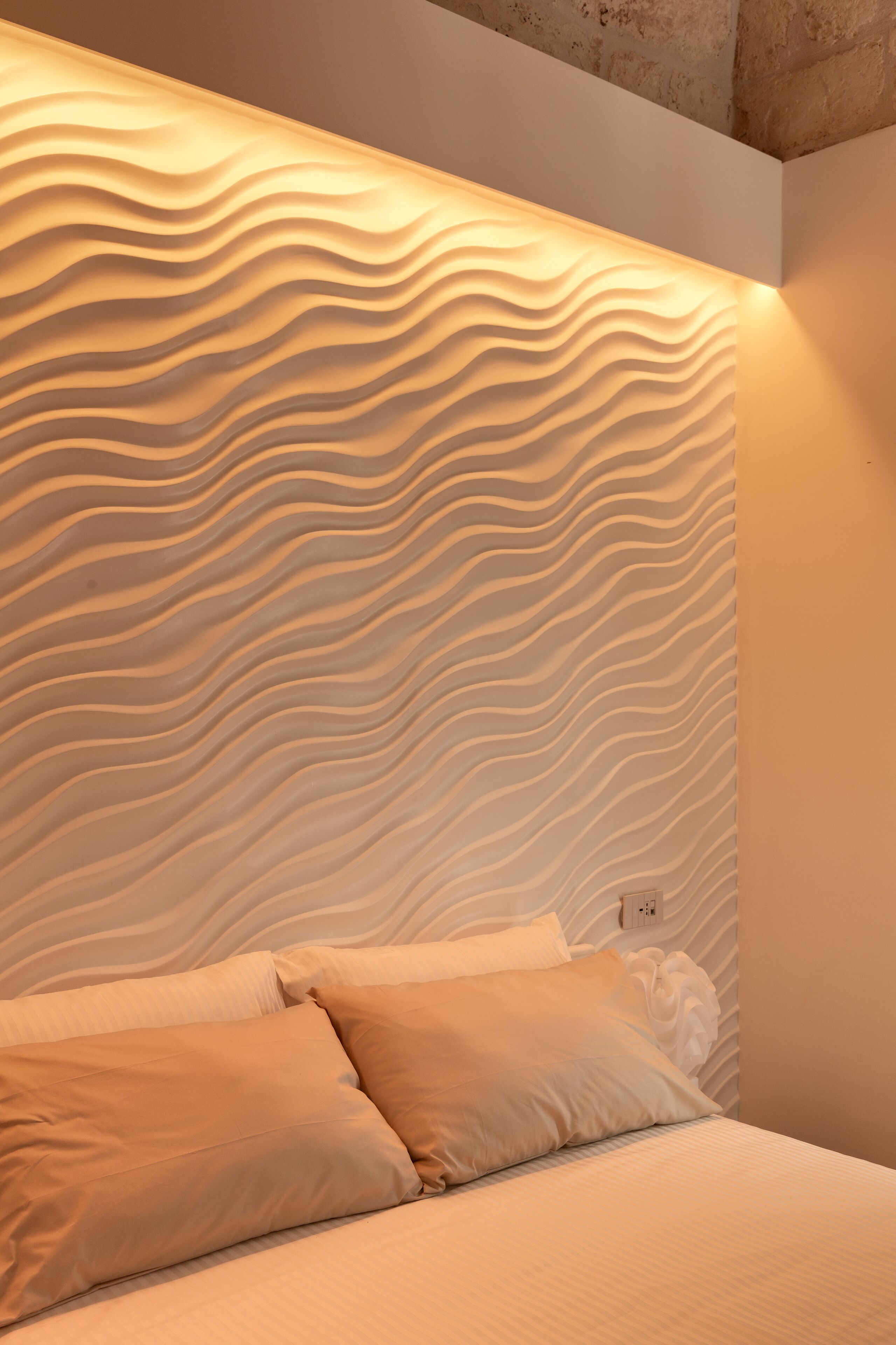Una camera da letto con un design murale testurizzato, un letto con biancheria bianca e una presa di corrente visibile.