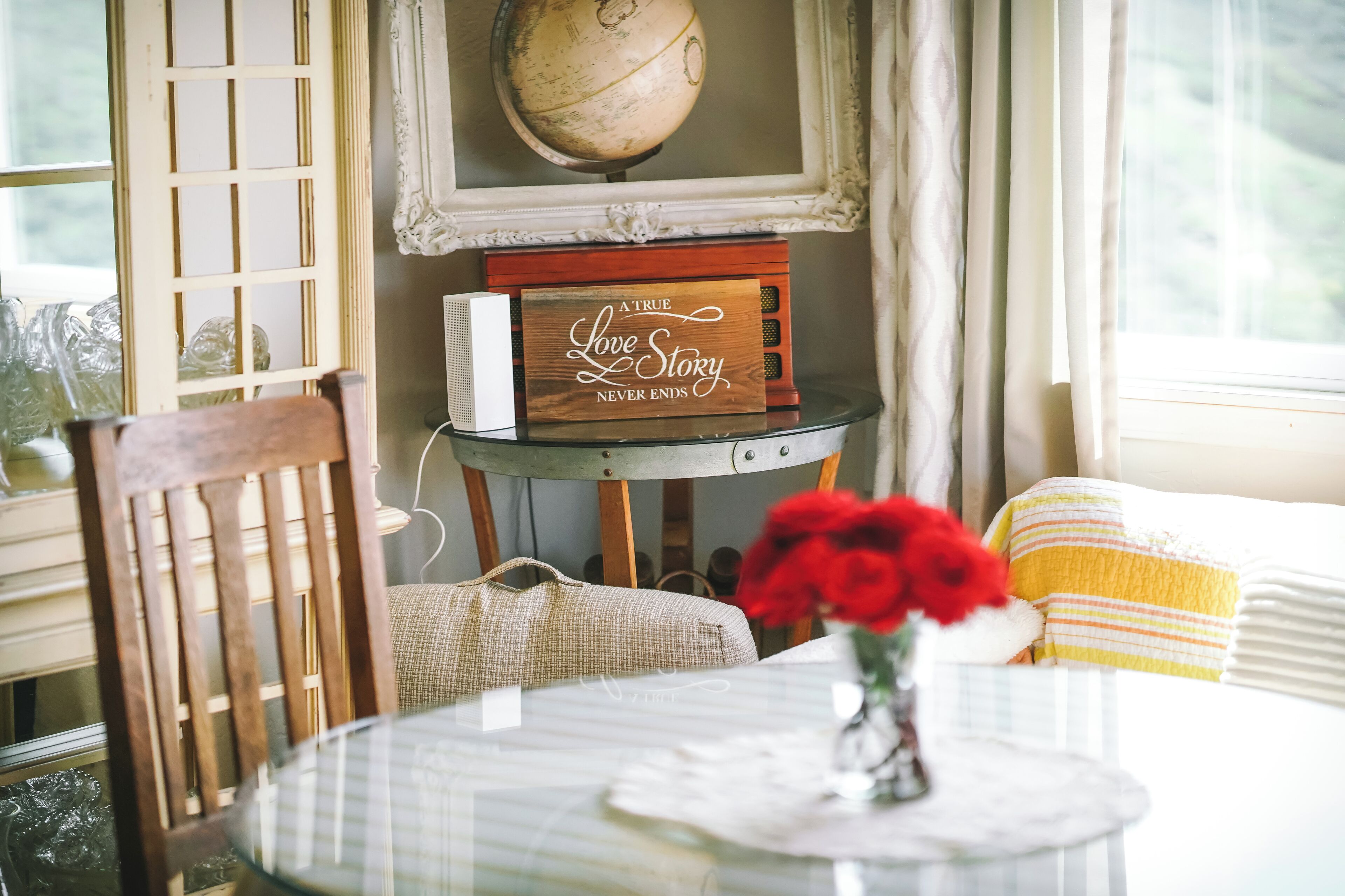 A cozy room with a round table, a wooden chair, a vase with red flowers, a globe on the wall, and a decorative box with a message.