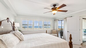 Una camera da letto con un letto grande, un ventilatore a soffitto e vista sull'oceano dalle finestre.