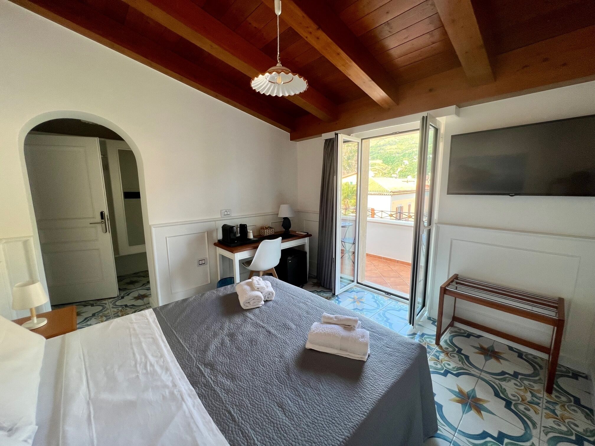 Ein Hotelzimmer mit Bett, Schreibtisch, Stuhl, Fernseher und einem Balkon mit Blick.