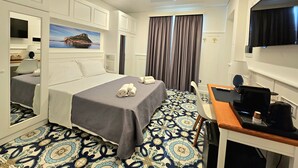 A hotel room with a bed, a desk with a computer, a TV, and a painting of a coastal scene. - Tea Luxury (Praia a Mare)