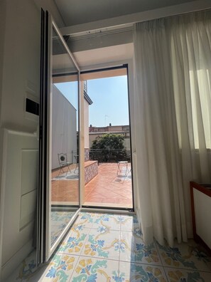 Una habitación con puerta de vidrio corredera que da a un patio exterior con suelo de baldosas, una pequeña mesa y sillas.