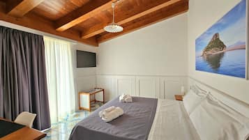 Ein Hotelzimmer mit Holzbalkendecke, einem Bett mit grauer Decke, einem Fernsehgerät an der Wand und einem Landschaftsbild.