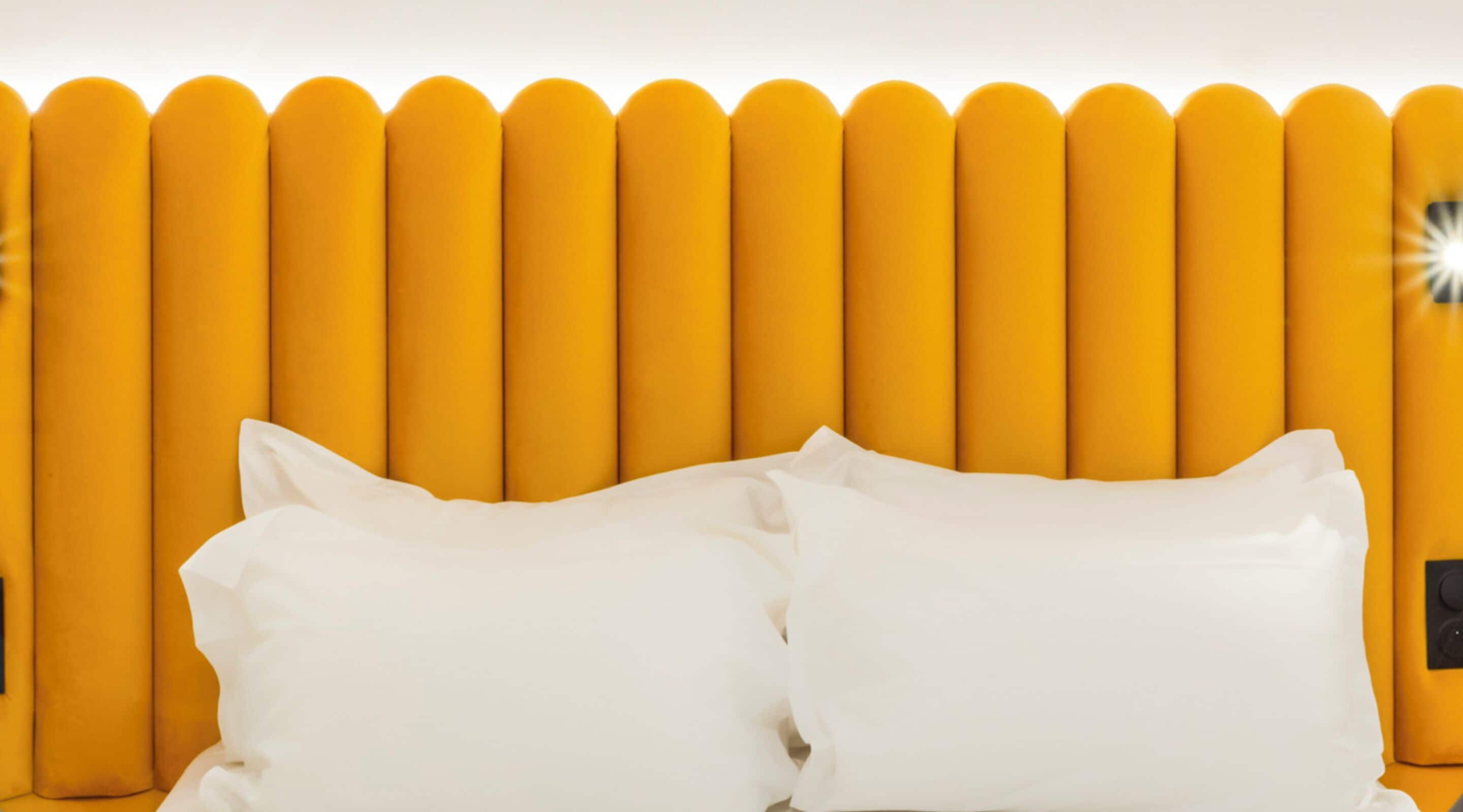 A bed with white pillows against a yellow headboard.