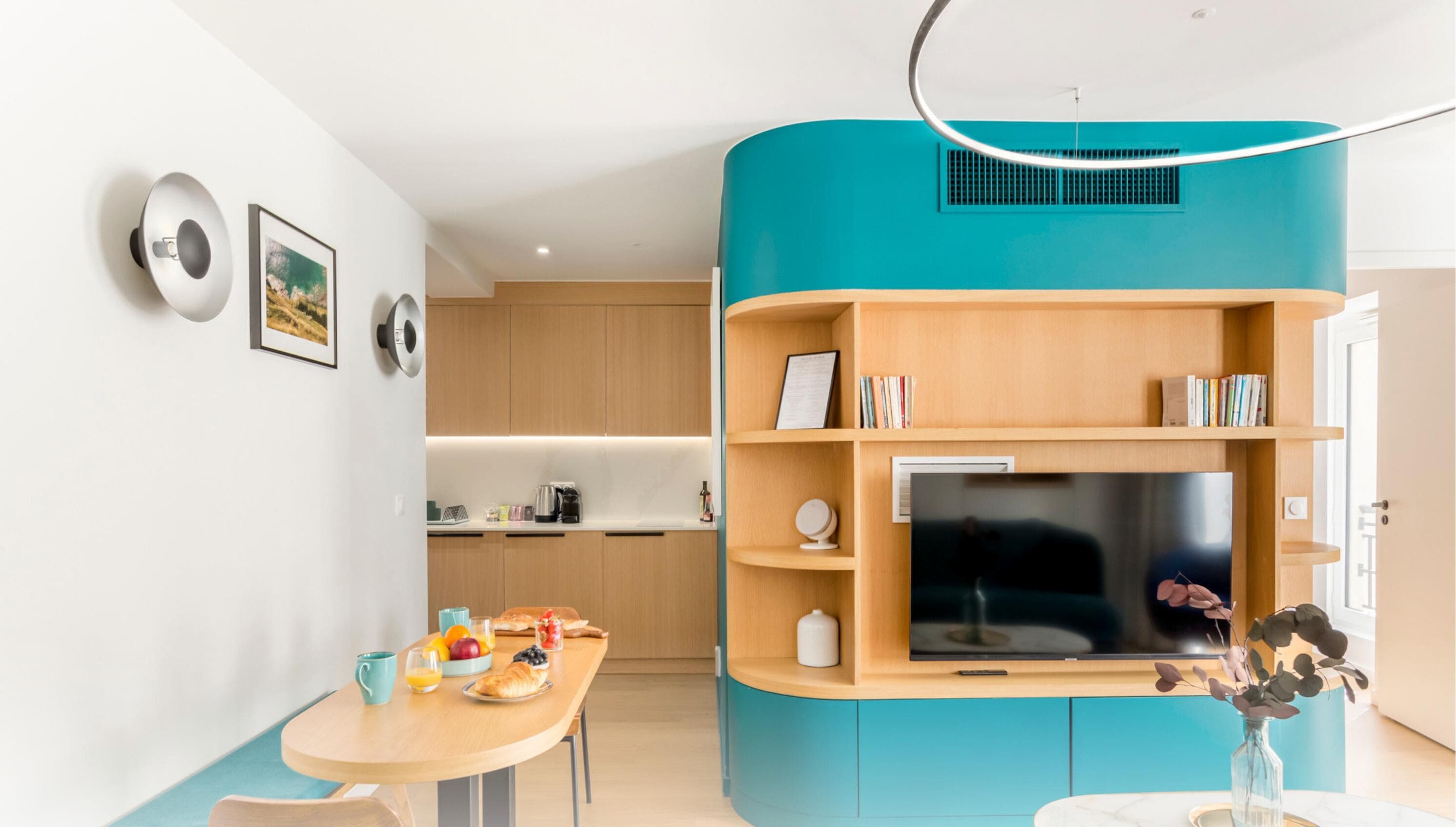 A modern living room with a large flat-screen TV, wooden shelving, and a dining area with breakfast items.