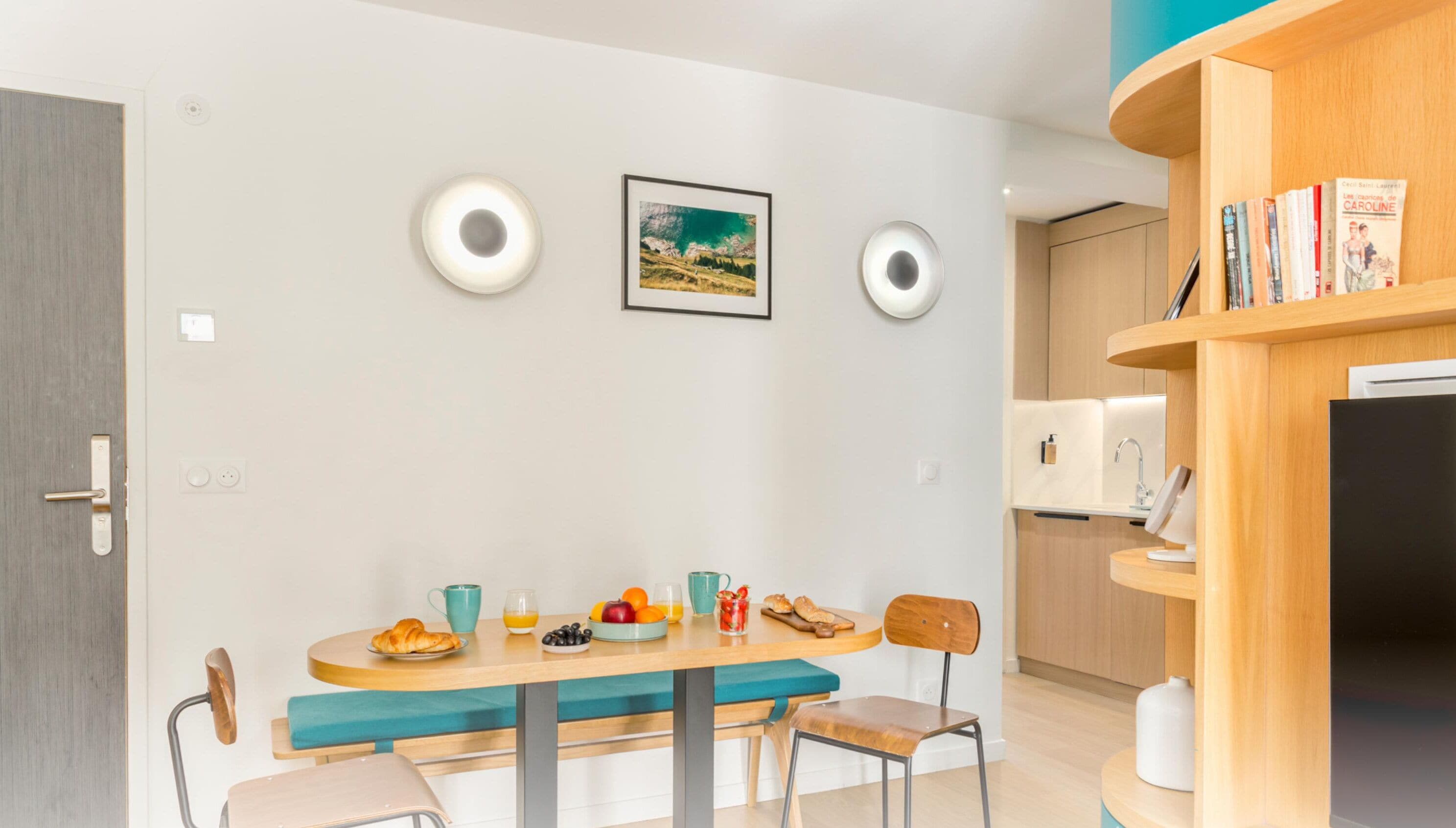 A modern kitchen with a dining table, chairs, and a bookshelf.