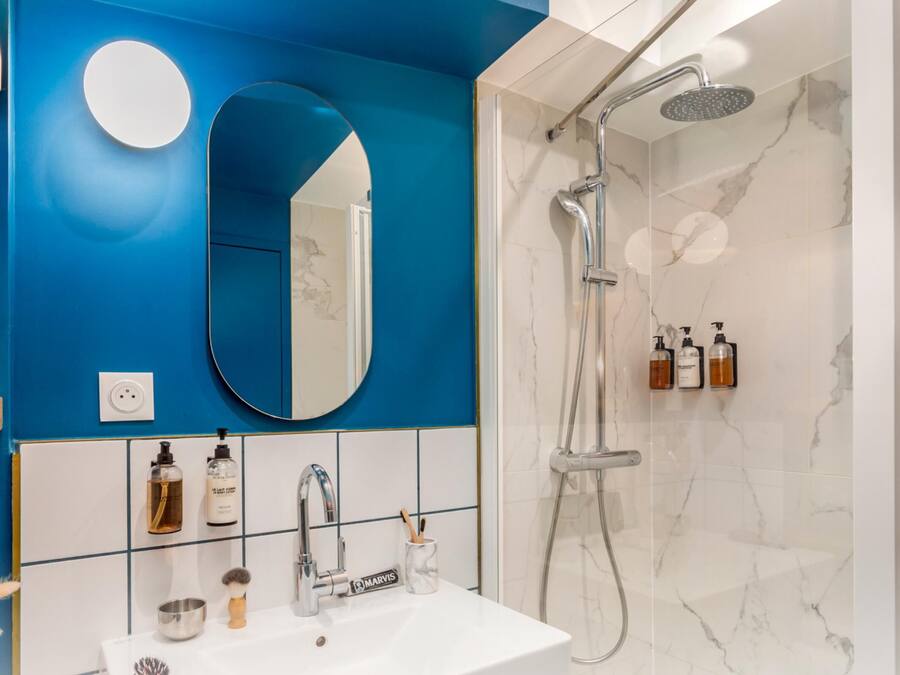 Um banheiro com parede azul, pia branca, espelho e chuveiro.