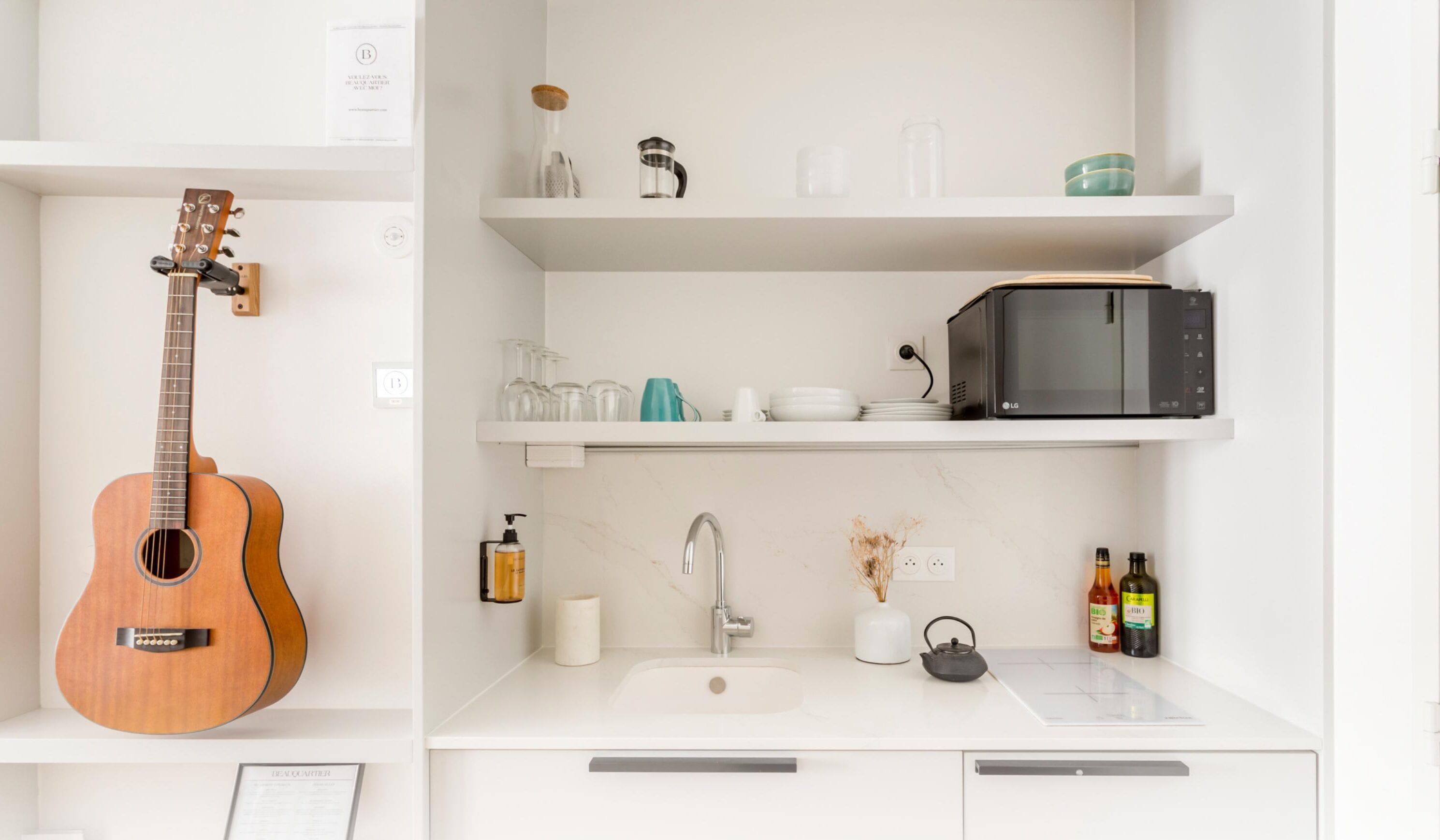 A kitchen with a guitar, a microwave, and various kitchen items on shelves.