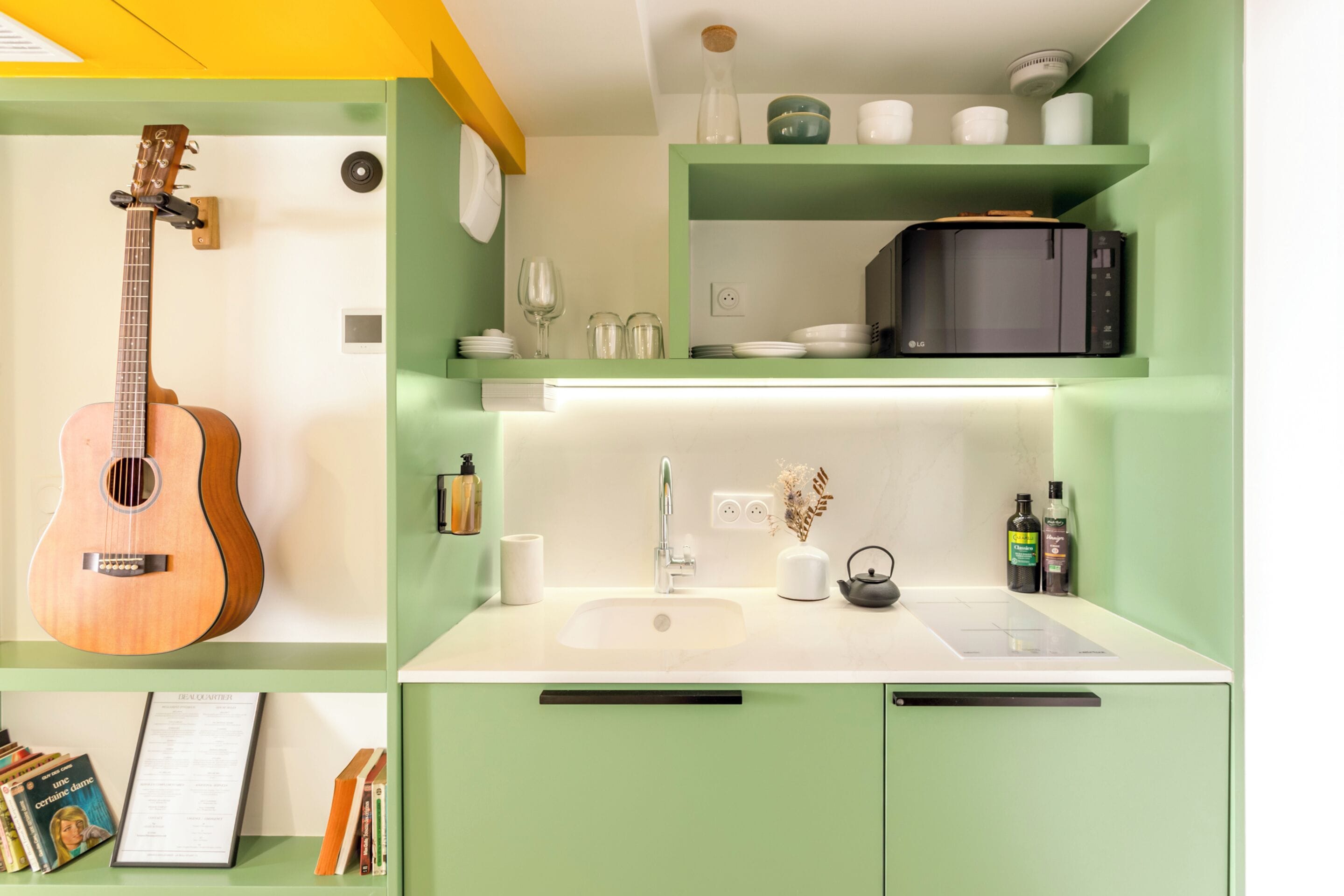 A kitchen with a built-in microwave, sink, and a guitar on the wall.