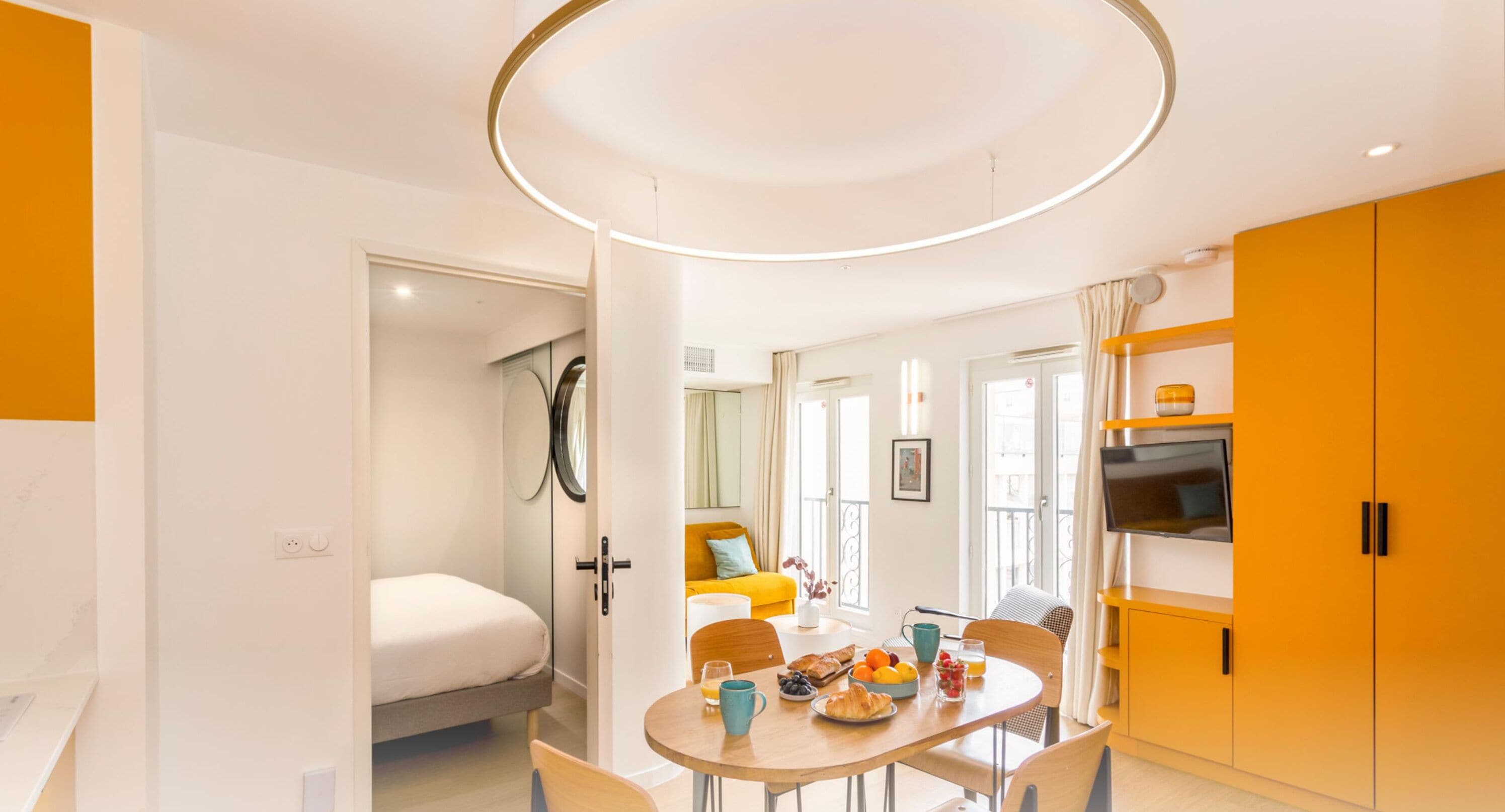 A modern hotel room with a dining area, a bed, and a TV.