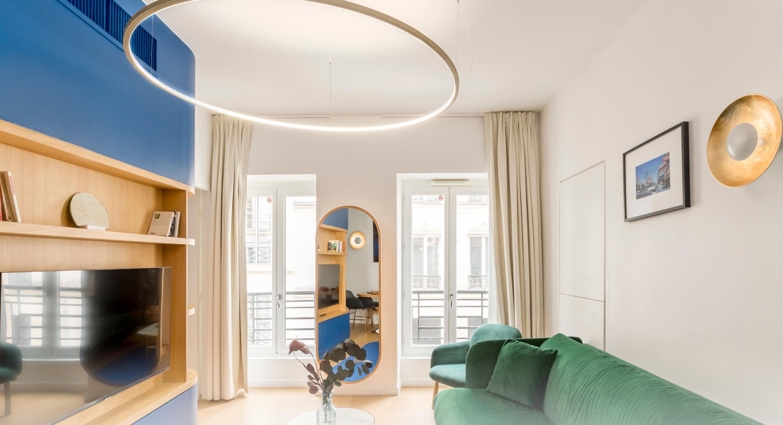Un salon moderne avec un téléviseur à écran plat, un canapé vert et un grand miroir.