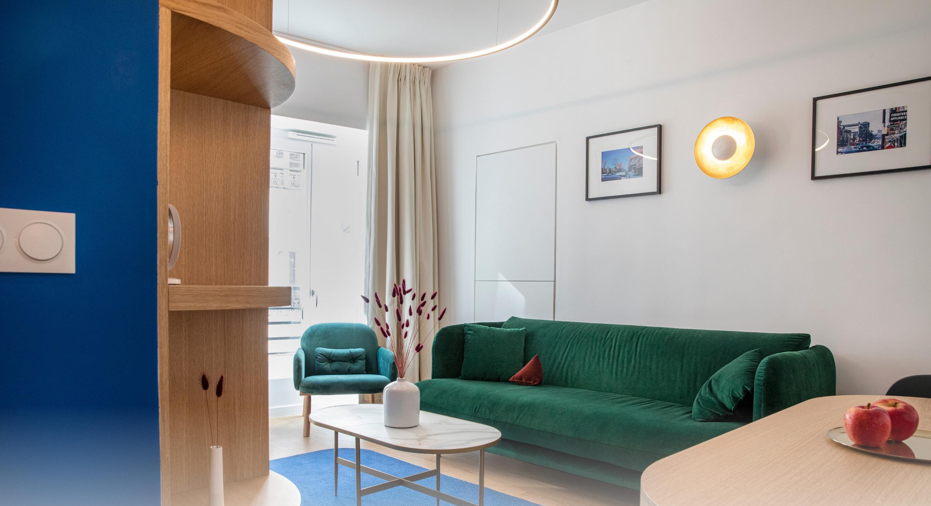 Una sala de estar moderna con un sofá verde, un sillón azul verdoso y una mesita con un florero.