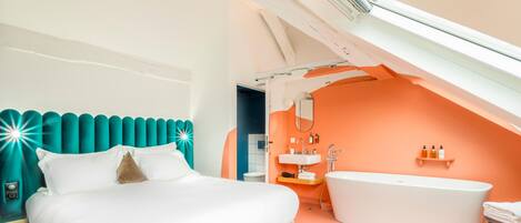 Un dormitorio moderno con una cama grande, un baño con bañera y un techo inclinado.