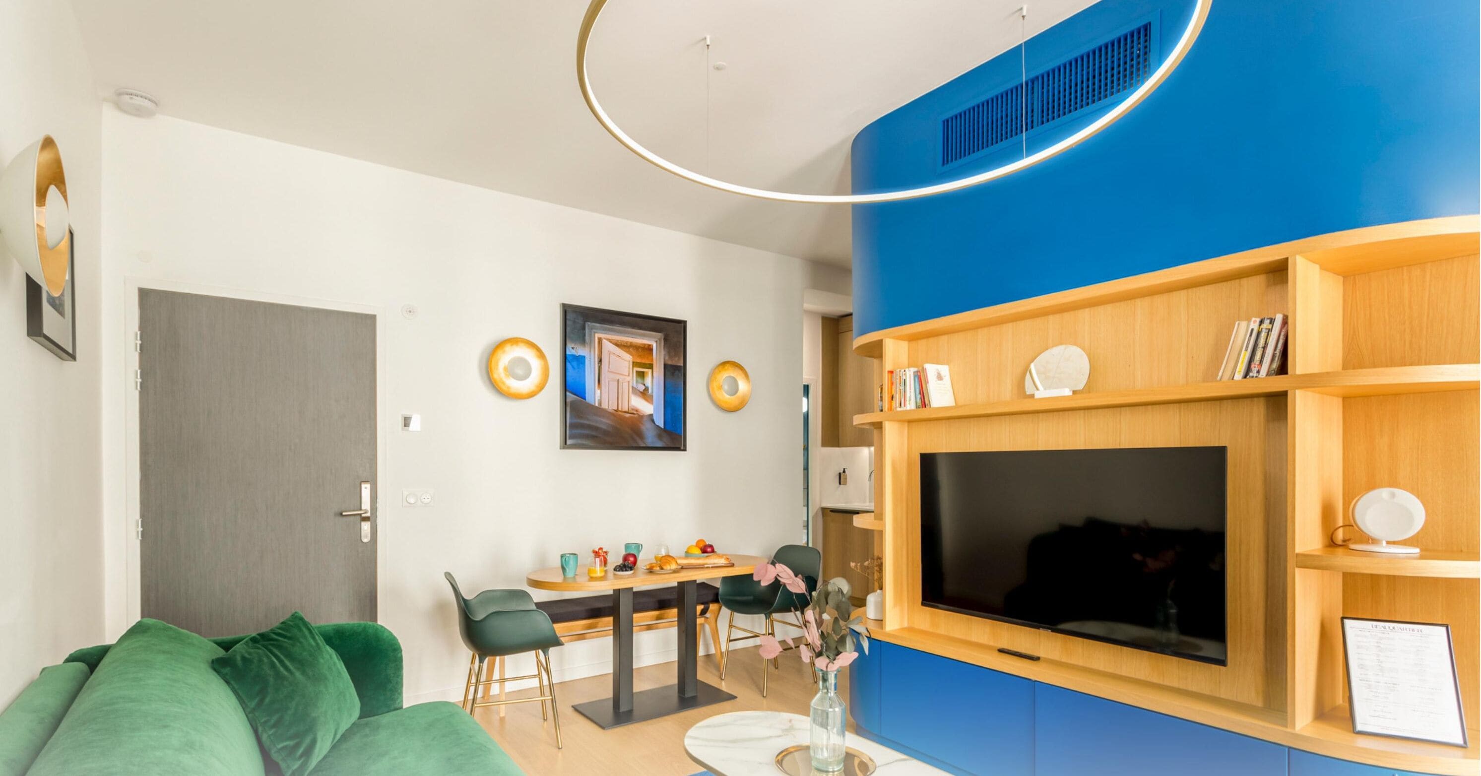 Een moderne woonkamer met een eethoek, een grote flatscreen-tv en een blauwe accentmuur.