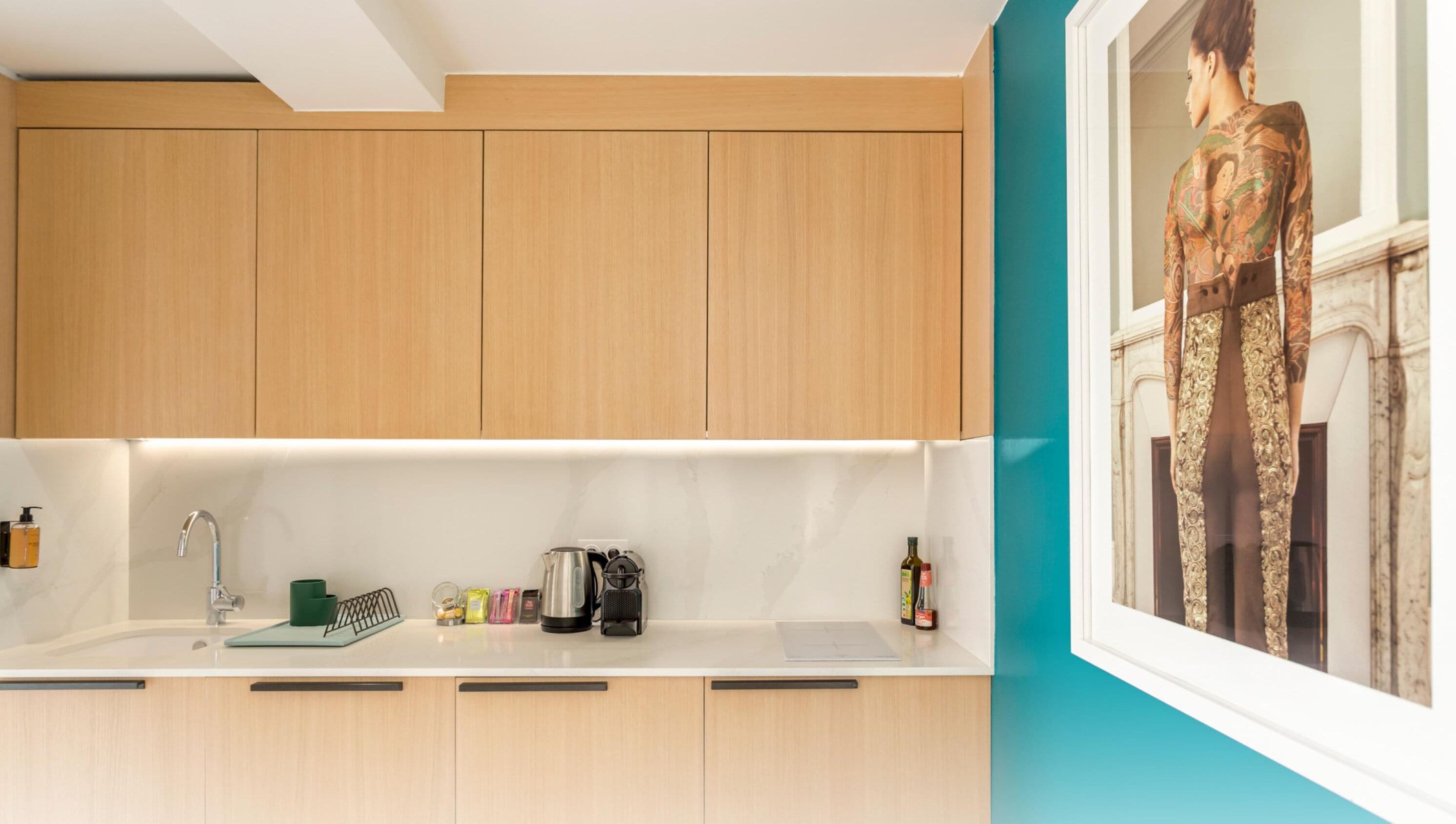 Een moderne keuken met houten kasten, een wit aanrechtblad en een muur in teal kleur.