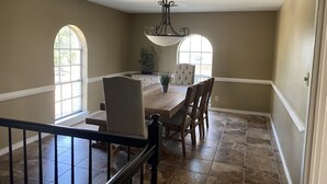 A dining area with a wooden table, four chairs, a chandelier, and two windows. - Spacious Split-Unit Home in Nassau Bay, Texas (Houston)